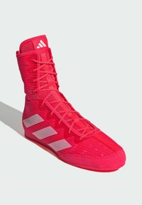 Scarpa sportiva rossa con design alto, tomaia in mesh testurizzato e tre strisce bianche. Presenta una chiusura con lacci e suola gomma.