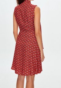 Red floral sleeveless dress with a fitted bodice and flared skirt. Features a high neckline and delicate white and blue patterns throughout.