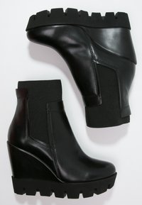 Botas de tobillo con cuña negra, con una parte superior de cuero suave, panel elástico en el costado y suela de goma texturizada con un borde dentado.