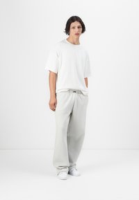 Hvit oversized t-skjorte laget av bomull, sammen med lysegrå joggebukser med snøring. Casual sko fullfører antrekket.