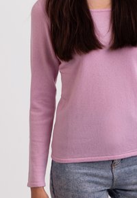 Helles rosa Langarmshirt aus einem weichen Material, mit Rundhalsausschnitt und taillierter Silhouette, kombiniert mit blauen Jeans.