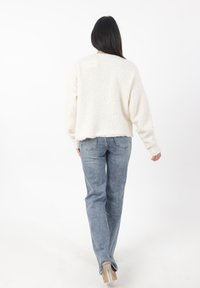 Maglione color crema, strutturato e con un design cropped. Abbinato a jeans straight-leg azzurri chiari, con un sottile motivo scolorito.