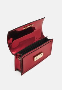 Pochette en cuir verni rouge avec une finition brillante, présentant une forme rectangulaire, une bordure noire et un fermoir en métal doré. L'intérieur comprend une poche zippée.