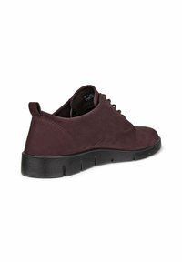 Scarpe basse in suede bordeaux con punta rotonda, suola nera testurizzata e allacciatura anteriore; dotate di un pratico tab sulla parte posteriore.