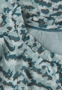 Tessuto azzurro chiaro con un motivo astratto in teal e marrone, che presenta un primo piano di un colletto arricciato e dettagli delle cuciture.