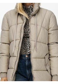 Beige puffjakke med lynlås og snore, båret over en leopardprintet top og mørkeblå høj talje jeans.