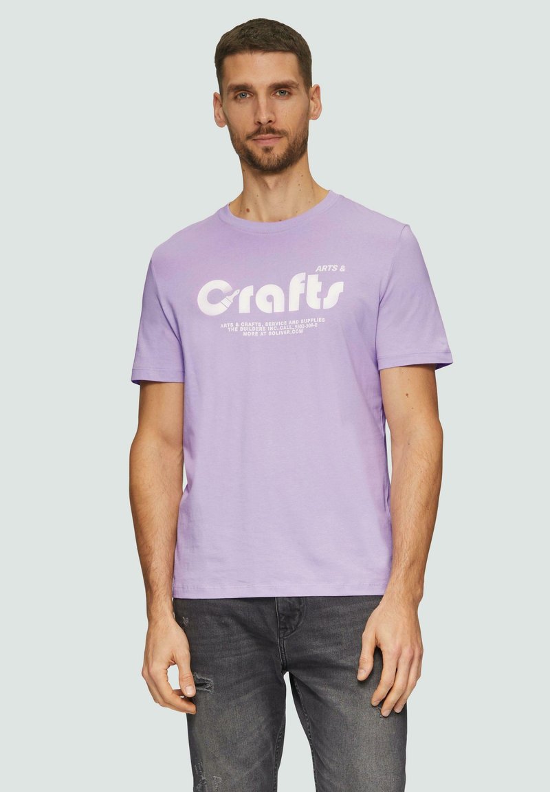 Licht paarse katoenen t-shirt met witte "Crafts" opdruk. Korte mouwen, ronde hals, relaxte pasvorm, gedragen met donkergrijze versleten jeans.
