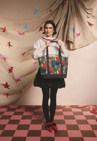 Kangaskassi, jossa vihreä tausta, värikkäät sienikuvioinnit ja ympyräkuviot sekä musta pohja. Varustettu tukevilla mustilla kahvoilla.