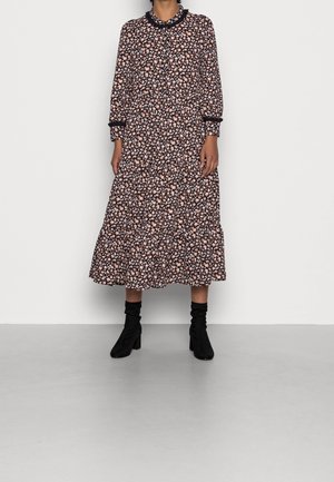 Personne portant une robe longue à manches longues jusqu'aux chevilles, avec une base noire et un motif floral rose, associée à des bottes noires à talons mi-mollet.