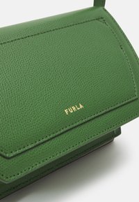 Zelená kožená taška s texturovaným povrchem, zdobená zlatým logem a strukturovaným designem. Detaily zahrnují precizní šití a klopový uzávěr.