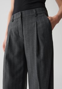 Pantalons rayés gris en tissu tissé, dotés de plis à l'avant, de poches latérales et d'une coupe cintrée à la taille.