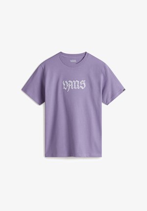 Ogrodniczki z denimu mają regulowane ramiączka i kieszeń z przodu, w połączeniu z jasnofioletowym t-shirtem z grafiką oraz czarno-białymi sneakersami.