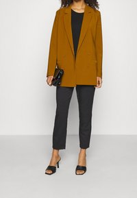 Brun dubbelknäppt kavaj med slag, matchad med svart topp och byxor. Accessoar: liten svart kuvertväska; skor med blockklack.