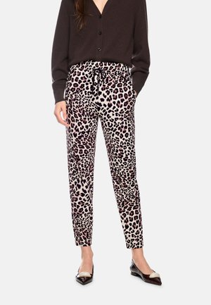 Woman wearing leopard print tapered pants with a drawstring waist, black buttoned cardigan, and black pointed shoes with cream accents.