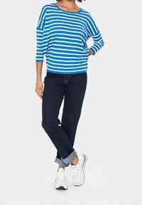 Modrý a bílý pruhovaný svetr s kulatým výstřihem, doplněný tmavými džínami s vyhrnutými manžetami a bílými teniskami.