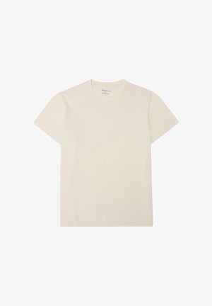 Camiseta beige de manga corta con cuello redondo y texto logo blanco minimalista centrado en el pecho, mostrada extendida sobre fondo blanco.