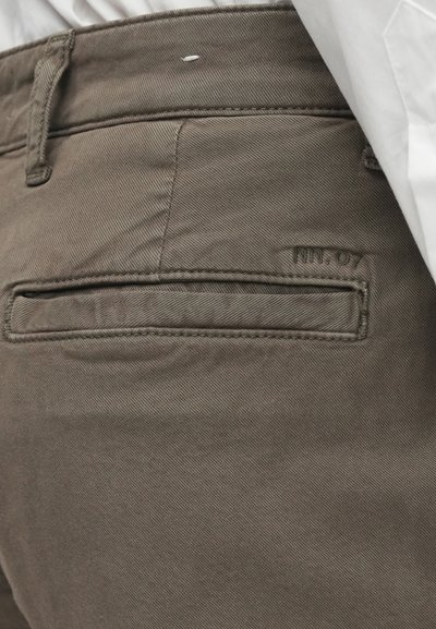 Καφέ, υφασμάτινα παντελόνια πλεγμένα με οριζόντια υφή. Διαθέτουν μια πίσω τσέπ η με καπάκι και διακριτική επωνυμία ραμμένη στο πλάι.