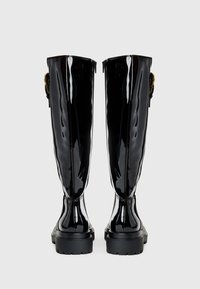 Zwarte glanzende laarzen tot de knie met een robuuste zool, met een ritssluiting aan de achterkant en versierde gouden hardware accenten.