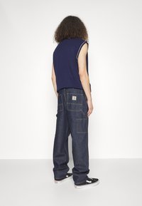 Navy sleeveless top paired with dark denim cargo pants featuring multiple pockets, prominent stitching, and a branded label on the back.