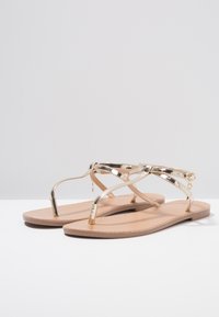 Guldmetalliska flip-flopsandaler med platta sulor och en tunn remdesign. Har en överlappande rem och subtil accenthårdvara.
