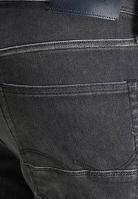 Jeans de mezclilla negra con un bolsillo trasero con sutiles detalles de costura y una etiqueta de cuero suave en la cinturilla.