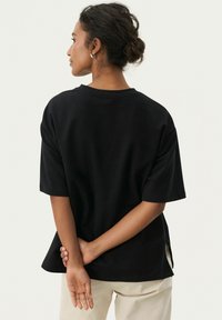 Camiseta negra de manga corta con escote redondo y aberturas laterales, hecha de una mezcla de algodón, con un ajuste relajado.