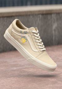 Beige canvas sneaker with white rubber sole, featuring floral embroidery including a lemon and leaves on the side, and white laces.