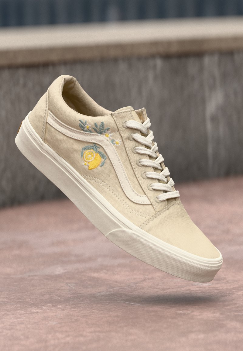 Beige canvas sneaker with white rubber sole, featuring floral embroidery including a lemon and leaves on the side, and white laces.