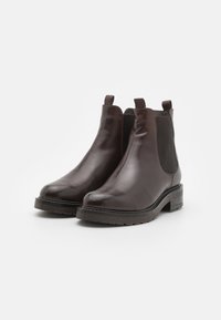 Bottes Chelsea en cuir brun avec des panneaux élastiques sur les côtés, bout rond, petit talon carré et languettes pour un enfilage facile. Texture lisse tout au long.