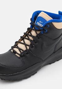 Černé a béžové vysoké tenisky s texturovaným svrškem z kůže a syntetického materiálu, černými tkaničkami a modrým logem Nike na jazyku.