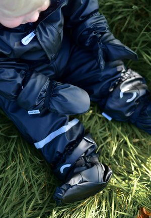 Schwarzer wasserdichter Schneeanzug mit elastischen Bündchen, reflektierenden Streifen und befestigten Fäustlingen, getragen beim Sitzen auf grünem Gras.