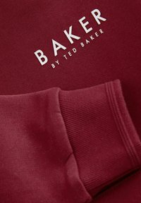 Felpa bordeaux con texture morbida, caratterizzata dal logo bianco "BAKER" di Ted Baker. Include polsini a costine e una finitura in tessuto liscio.
