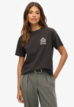 T-shirt en coton noir à manches courtes et col rond, avec un logo et un emblème Superdry blancs sur le côté supérieur gauche.