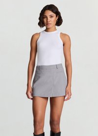White ribbed tank top paired with a gray mini skirt featuring a smooth texture and side pockets. Model stands against a neutral background.