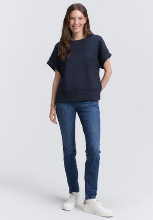 Navy blue women's sweatshirt with short sleeves and a relaxed fit, paired with blue denim jeans and white sneakers. Smooth texture, casual style.