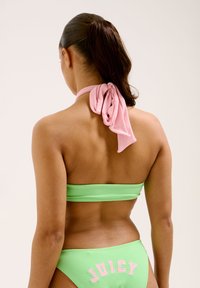 Bikini verde con top a bandeau e fondo coordinato, con un fiocco rosa al collo e la scritta 'JUICY' ricamata in rosa sul retro.