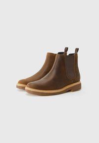 Brown leather Chelsea boots with elastic side panels, contrast stitching, and a flat rubber sole. Features pull tabs for easy wear.
