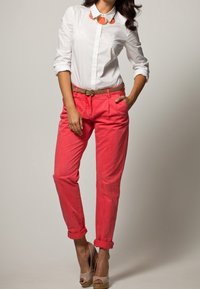 Vit skjorta med uppvikta ärmar, tillsammans med klara korallfärgade byxor och ett tanfärgat bälte. Outfiten inkluderar ett geometriskt halsband och tanfärgade plattformsskor.