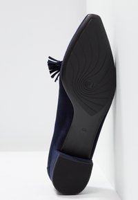 Marineblauwe suède schoen met een kwastdetail, zwarte gestructureerde rubberen zool en een licht gebogen hak, die een gladde afwerking toont.