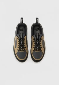 Sorte og brune sneakers med en teksturert overdel, nettingpaneler, flate sorte snørebånd og løftestropper på hælene for enkel påkledning.