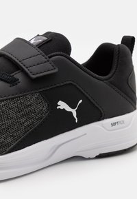 Chaussure de sport noire avec un panneau en mesh texturé, une bande Velcro, une semelle blanche et un logo de chat blanc sur le côté ; dotée d'un rembourrage doux.