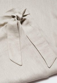 Tissu en lin beige clair avec un détail de nœud noué, présentant une texture lisse et des fibres naturelles subtiles. Bords plats accentués.