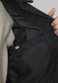 Tissu extérieur en laine grise avec une doublure intérieure noire lisse. Comprend une fermeture éclair et une petite étiquette à l'intérieur. Accents de texture polaire visibles.