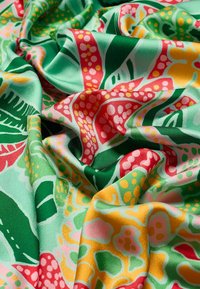 Tissu coloré avec une finition brillante, arborant des motifs floraux vibrants dans des nuances de vert, rose, rouge et jaune. Texture douce et drapée.