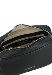 Borsa cosmetica in pelle nera con superficie testurizzata, dotata di zip argentata e rivestimento in tessuto beige con tasche interne.