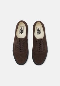 Braune Wildleder-Sneaker mit schwarzen Gummisohlen, runden Schnürsenkeln, klassischem Low-Top-Design und einem Logo auf der Zunge.