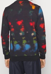 Sudadera negra con patrones abstractos multicolores en rojo, azul, verde y amarillo. Presenta un cuello y puños acanalados, fabricada con un tejido suave.