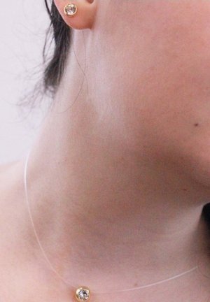 Gouden studoorbellen met heldere kristallen op een blote nek, met een delicate transparante ketting zichtbaar onder de oorbellen.