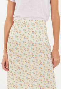 Jupe fleurie avec une base crème claire ornée de motifs floraux colorés en bleu, rouge et jaune, fabriquée en tissu léger.