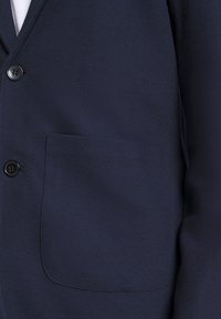 Navy blue blazer in textured fabric, featuring a single button closure and a front patch pocket. Smooth texture with subtle pattern.